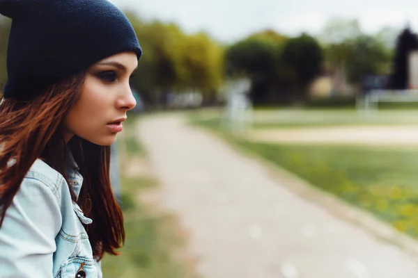 Portrait of a beautiful girl in a cap and a denim jacket sitting — Stock Photo, Image