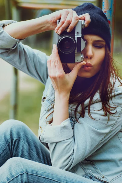 Portret pięknej hipsterki w czapce i dżinsowej kurtce z aparatem fotograficznym robiącym zdjęcia — Zdjęcie stockowe