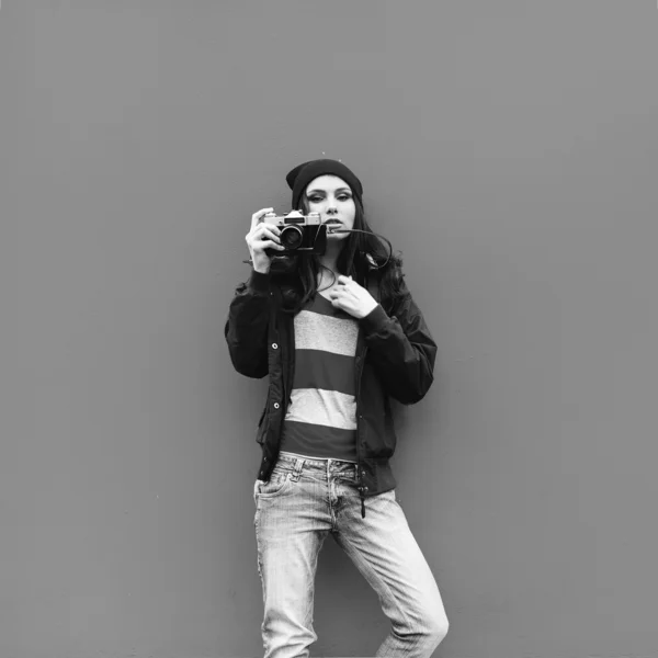 Ασπρόμαυρο πορτρέτο του ένα πανέμορφο hipster κορίτσι με μια φωτογραφική μηχανή στο παρασκήνιο — Φωτογραφία Αρχείου