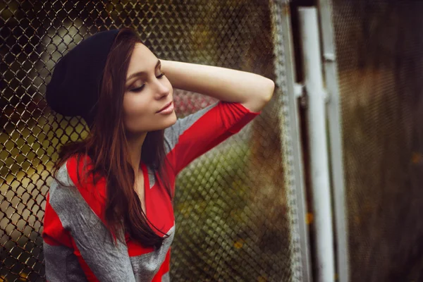 Portret van een mooi meisje in een hippe hoed en gestreepte jas op straat bij de poort buiten — Stockfoto