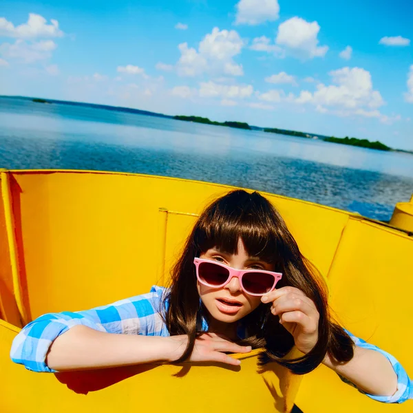 Retrato de una hermosa chica con una camisa azul y gafas de color rosa en una pared naranja y cielo azul — Foto de Stock