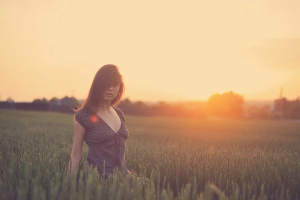 Junge Frau steht auf einem Weizenfeld mit Sonnenaufgang auf dem Rücken — Stockfoto