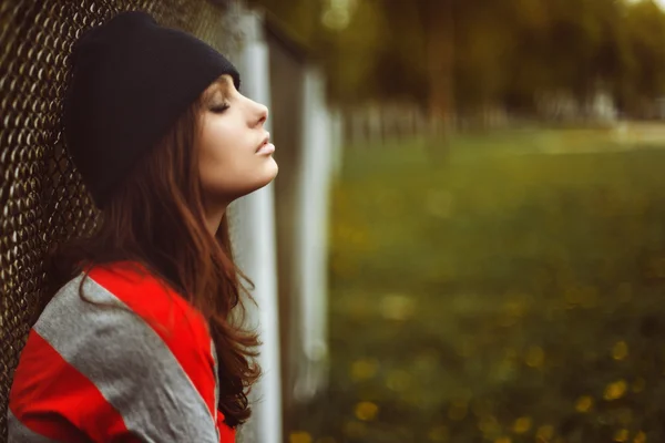 Portrait of a beautiful girl in a hipster hat and striped jacket at the gate outdoor — Stock Photo, Image