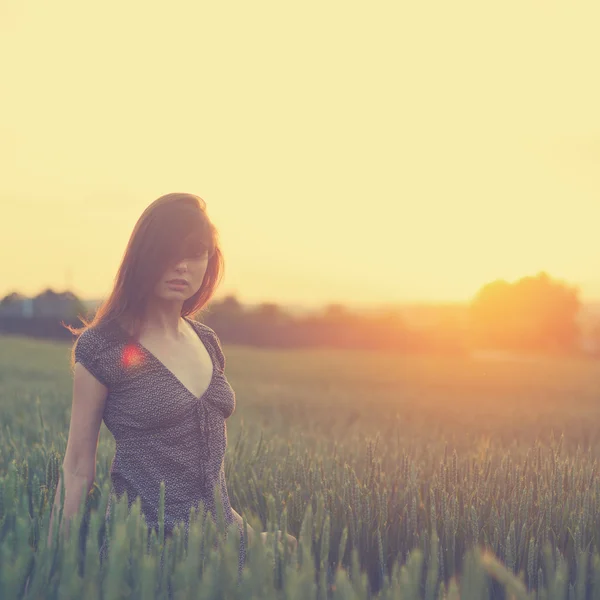 Junge Frau steht auf einem Weizenfeld mit Sonnenaufgang auf dem Rücken — Stockfoto