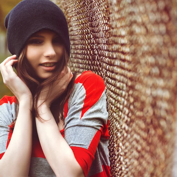 Portrait of a beautiful girl in a hipster hat and striped jacket  at the gate outdoor — Stock Photo, Image