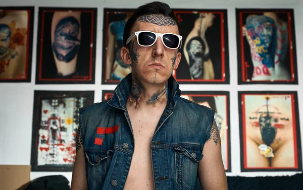 Homme tatoué en gilet denim et lunettes de soleil en studio — Photo