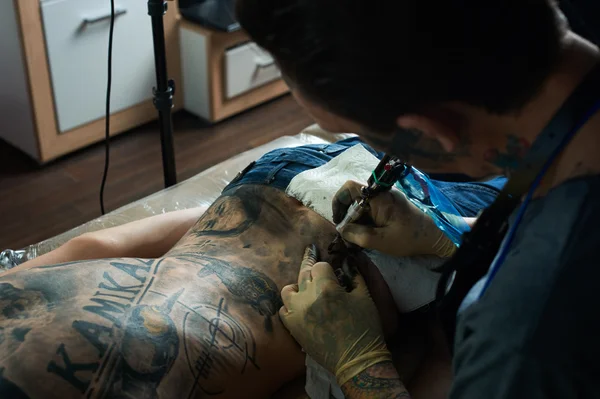Tattooist makes a tattoo on the back of a guy — Stock Photo, Image