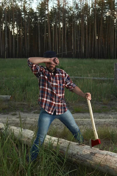 Skäggiga lumberjack innehar en stor yxa i hand och torkar svetten — Stockfoto