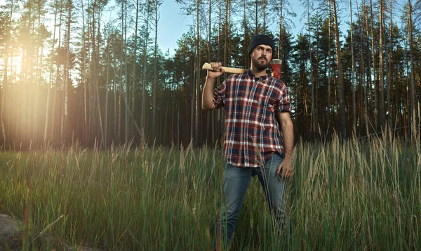 Skäggiga skogshuggare i hatt innehar en stor yxa på axel i fores — Stockfoto
