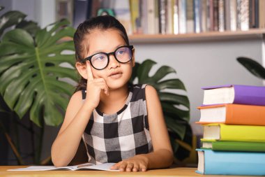Asyalı kız evde ders çalışıyor, masada kitaplarla oturuyor..