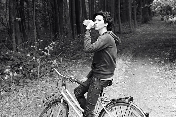 Young beautiful girl on a bicycle with a bottle of water in hand in the woods. Walking on a bicycle in the forest. A slim woman with a sports body shape on a bicycle.