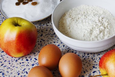 Mutfak masasında elmalı turta için malzemeler. Un, şeker, Kuru üzüm, yumurta ve ev yapımı hamur işleri için elma.