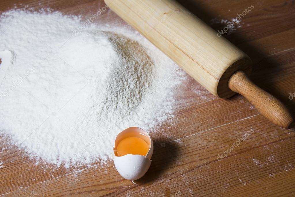 Ingredients for cooking dough on a wooden table. Flour, egg and a rolling pin.