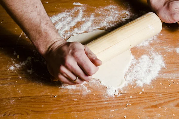 Man's hands rolled dough with wooden rolling pin on the wooden table. — Stock Photo, Image