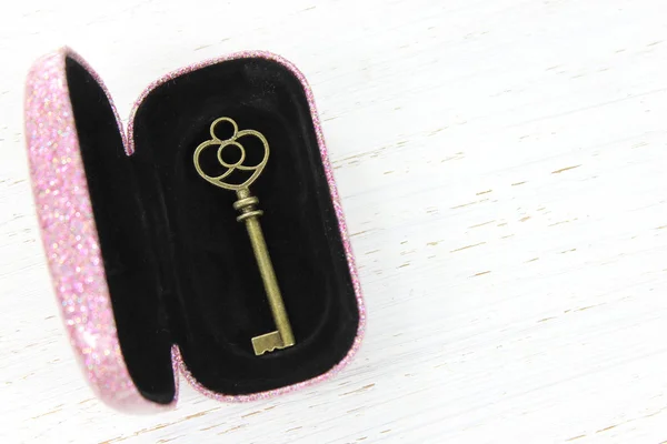 Antique brass key in glittery pink case on white distressed wood — Stock Photo, Image