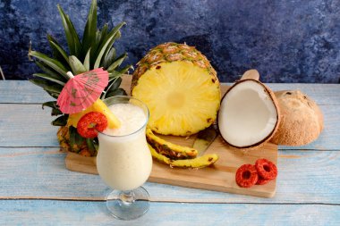Pina colada, tropikal kokteyl. Bir bardak pina colada mavi ahşap bir masa üzerinde kokteyl bileşenleri arka planda.