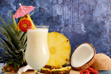Pina colada, tropikal kokteyl. Bir bardak pina colada mavi ahşap bir masa üzerinde kokteyl bileşenleri arka planda.