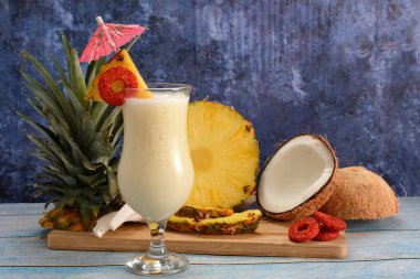 Pina colada, tropikal kokteyl. Bir bardak pina colada mavi ahşap bir masa üzerinde kokteyl bileşenleri arka planda.