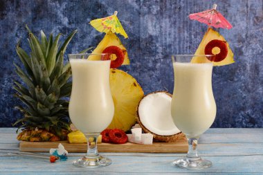 Pina colada, tropikal kokteyl. Bir bardak pina colada mavi ahşap bir masa üzerinde kokteyl bileşenleri arka planda.