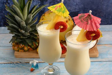 Pina colada, tropikal kokteyl. Bir bardak pina colada mavi ahşap bir masa üzerinde kokteyl bileşenleri arka planda.
