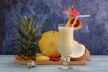 Pina colada, tropikal kokteyl. Bir bardak pina colada mavi ahşap bir masa üzerinde kokteyl bileşenleri arka planda.
