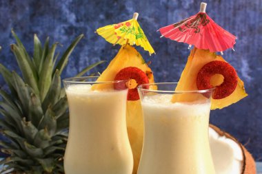 Pina colada, tropikal kokteyl. Bir bardak pina colada mavi ahşap bir masa üzerinde kokteyl bileşenleri arka planda.