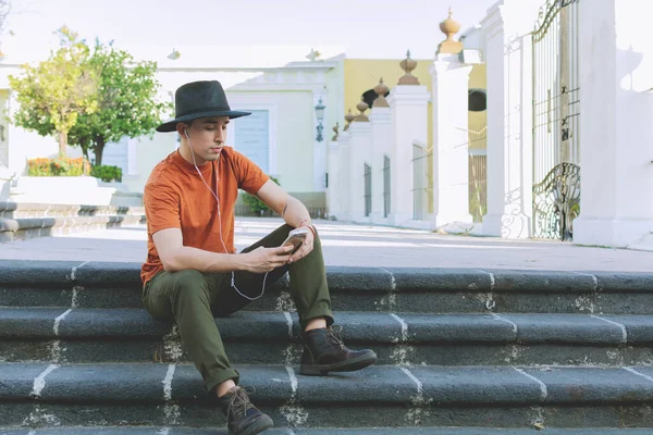 Young man sitting looking at the cell phone. Young person with hat.