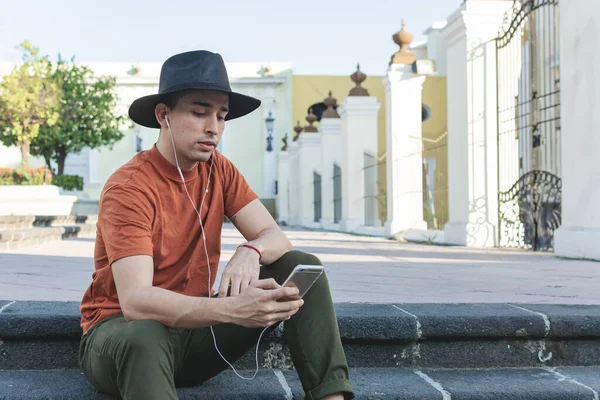 Genç adam cep telefonuna bakarak oturuyor. Şapkalı genç adam..