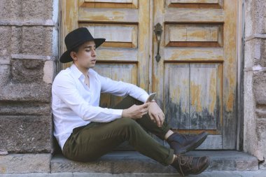 Genç adam cep telefonuna bakarak oturuyor. Şapkalı genç adam..