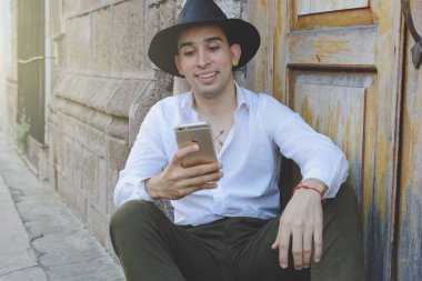 Genç adam cep telefonuna bakarak oturuyor. Şapkalı genç adam..