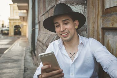 Genç adam cep telefonuna bakarak oturuyor. Şapkalı genç adam..