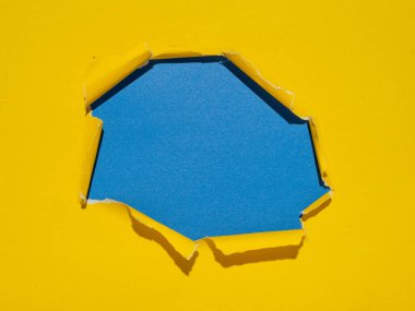 Torn hole in the center of a yellow paper on a blue background.