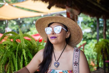 Hasır şapkalı ve güneş gözlüklü bir kadın portresi. Kameraya bakmıyor..