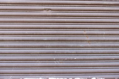 Eski ve sıkıntılı metal bir kepenk kapanıyor, aşınma ve yırtılma izleri var..