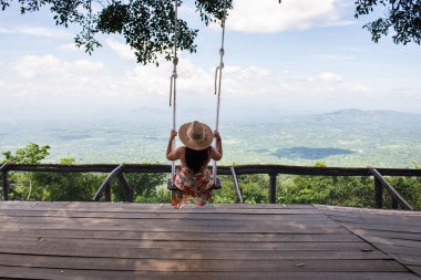 Serene Woman Swing with Straw Hat 'in Dağ Manzarasının keyfini çıkarıyor.