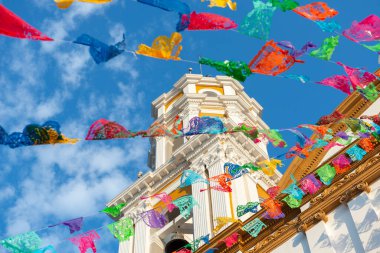 Mavi gökyüzüne karşı kesilmiş kağıtlarla süslenmiş şenlikli ve parlak bir kilise. Papel picado.