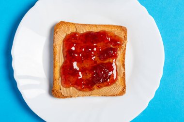 Fıstık ezmeli ve reçelli sandviçin üstü beyaz bir tabakta servis edilir.