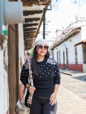 Mazamitla 'da büyüleyici bir sokakta duran siyah bir kazak, inci ve bere giyen bir kadının portresi.