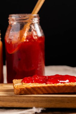 Fıstık ezmeli ve reçelli sandviç, ahşap bir tepside, arka planda her kavanozdan yayılmış.