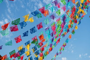 Mavi gökyüzüne asılı renkli şenlikli papel picado süslemeleri.