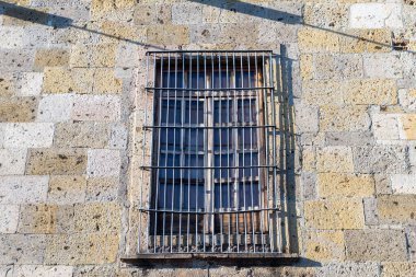 Eski bir binanın penceresini kaplayan metal ızgaralı taş bir duvarın yakın çekimi.