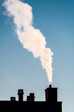 Konut binasının çatısındaki bacadan beyaz duman çıkıyor. Soğuk, ısınma ve kirlilik kavramları