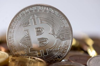 Bulanık paraların arasında duran gümüş bir bitcoin. Bitcoin bir kripto para birimi, merkezi bankası ya da tek bir yöneticisi olmayan, engelleme teknolojisini kullanan bir dijital para birimi.