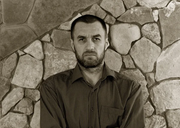 Portrait of a sullen unshaven white man in a striped shirt against the wall of stone. black and white photo — Stock Photo, Image