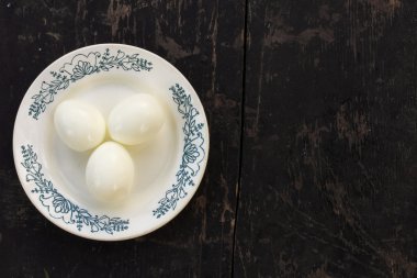 boiled chicken eggs without the shell on a ceramic saucer on a old wooden background black. with space for text clipart