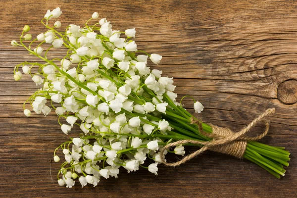 Konwalia bukiet białych kwiatów związany z ciąg na tle starych płyt szary stodoła w pęknięcia z bliska. — Zdjęcie stockowe