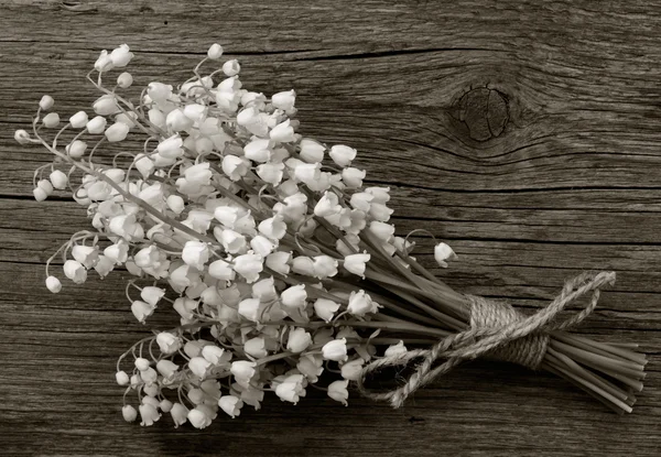 Lily of the valley bouquet of white flowers tied with string on a background of old gray barn boards in the cracks close up — Stock Photo, Image