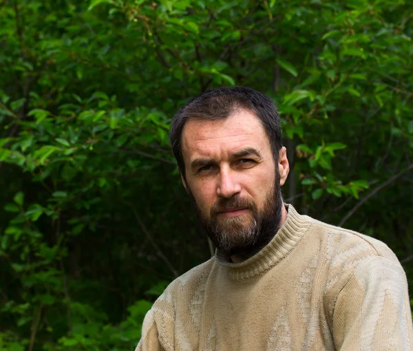 Retrato de um homem adulto pensativo com cabelos grisalhos em sua barba contra o pano de fundo da folhagem verde — Fotografia de Stock