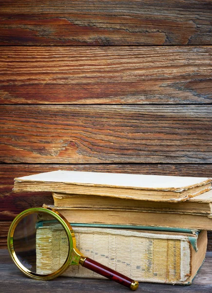 Una pila de libros antiguos y lupa sobre fondo de madera — Foto de Stock