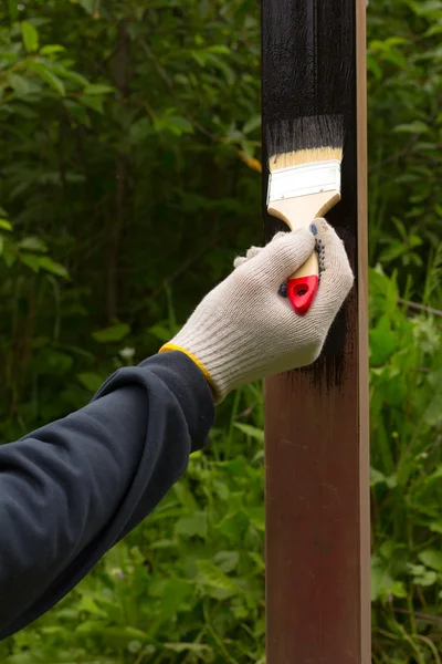 Hand i handske rag paint pensel brun stål pole i svart på en bakgrund av gröna blad — Stockfoto